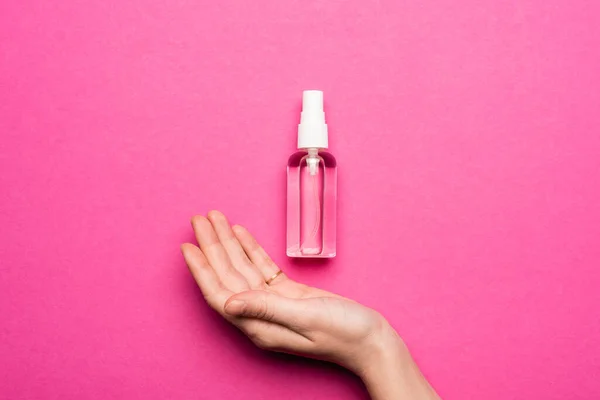 Cropped view of female hand near spray bottle with liquid antiseptic on pink — Stock Photo