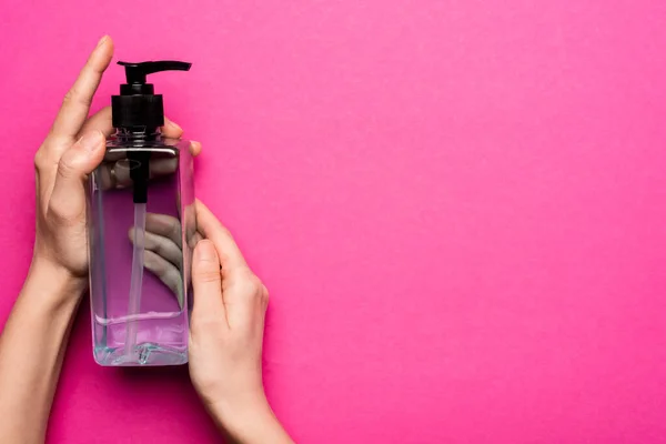 Vue recadrée de la femme tenant bouteille avec désinfectant pour les mains sur rose — Photo de stock