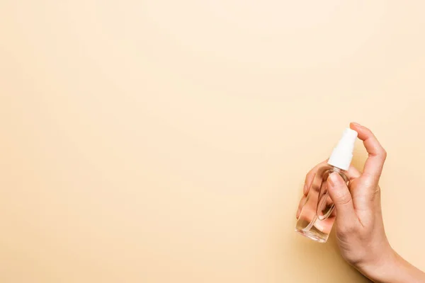 Partial view of woman spraying sanitizer from transparent bottle on beige — Stock Photo