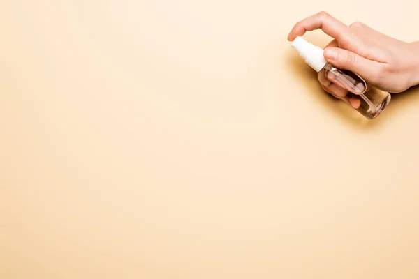 Vista parcial de la mujer pulverización de líquido antiséptico de botella transparente en beige - foto de stock