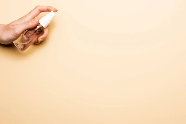 Cropped view of woman spraying antiseptic liquid from transparent bottle on beige — Stock Photo