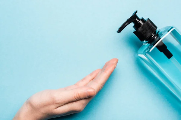 Частичный вид женской руки возле бутылки с дезинфицирующим средством на голубом — стоковое фото