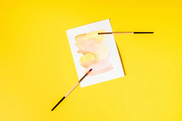 Top view of paintbrushes near painting on yellow — Stock Photo