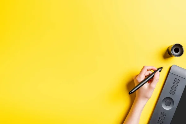 Ausgeschnittene Ansicht eines Designers, der Stift in der Nähe von Zeichnungstablette auf gelb hält — Stockfoto