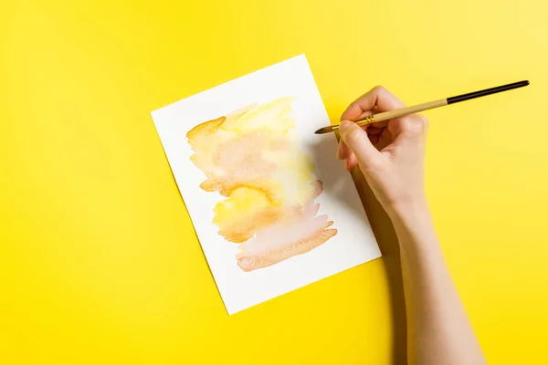 Cropped view of artist holding paintbrush near painting on yellow — Stock Photo