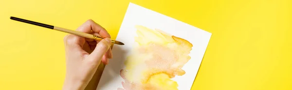 Horizontal crop of artist holding paintbrush near painting on yellow — Stock Photo