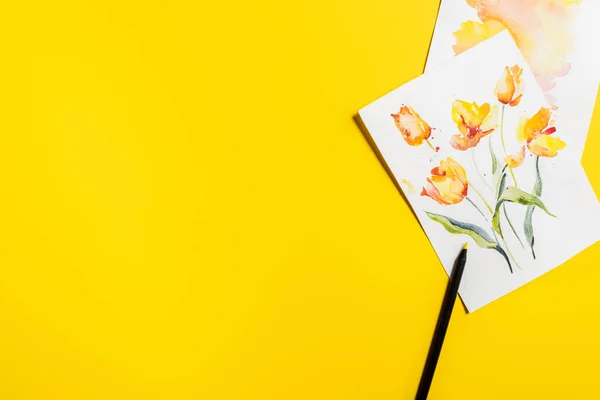 Top view of paintbrush near paintings with drawn flowers on yellow — Stock Photo