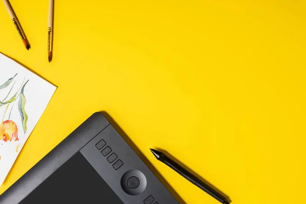 Вид зверху на пензлі біля живопису, малюнок планшета і стилуса на жовтому — стокове фото