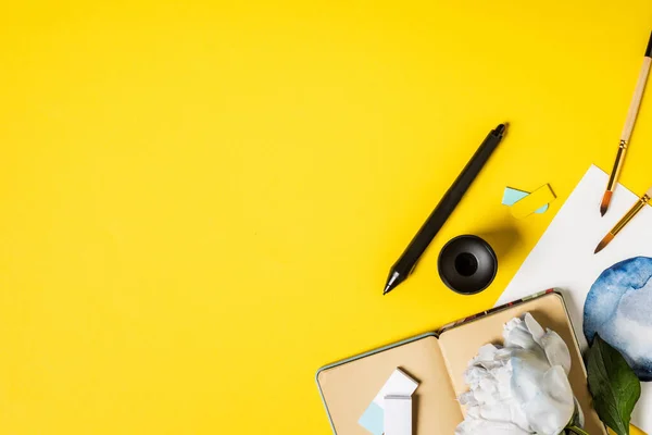 Pinsel in Malnähe, schwarzer Stift, Notizbuch und Blume auf gelb — Stockfoto