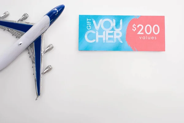 Top view of toy plane near gift voucher with 200 values sign on white background — Stock Photo