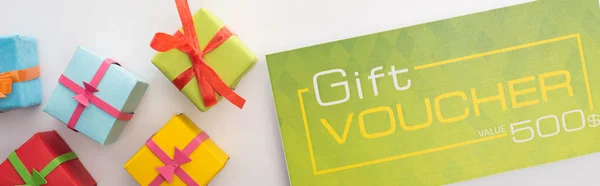 Panoramic shot of gift voucher near presents on white background — Stock Photo