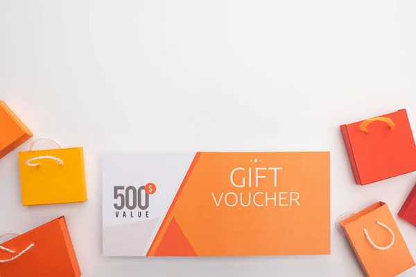 Top view of gift voucher with toy shopping bags on white background — Stock Photo