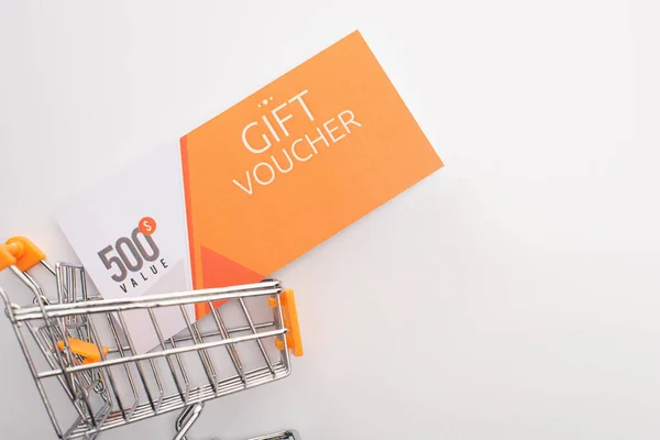 Top view of gift voucher with value lettering in toy shopping cart on white background — Stock Photo