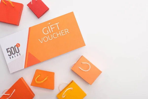 Top view of gift voucher near toy shopping bags on white surface — Stock Photo