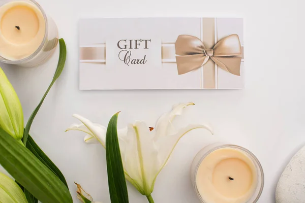 Вид сверху подарочной карты, лилия и свечи на белом фоне — стоковое фото