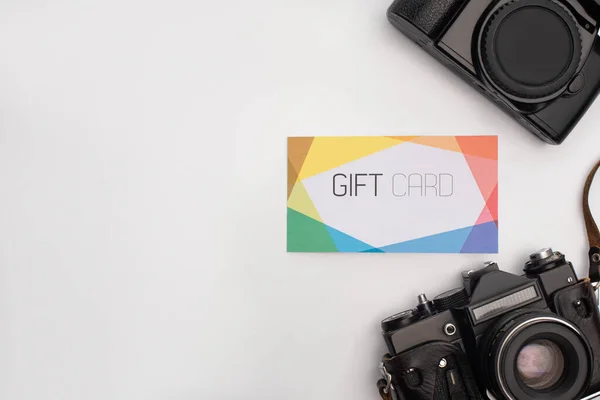 Vista dall'alto di fotocamere digitali vicino a gift card su sfondo bianco — Foto stock