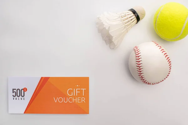 Top view of gift voucher near shuttlecock, tennis and cricket balls on white surface — Stock Photo