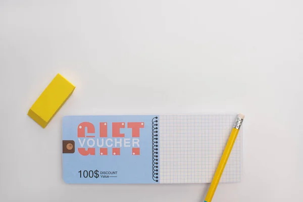 Vue du dessus du crayon et de la gomme près du bon cadeau sur fond blanc — Photo de stock