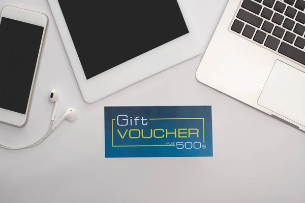 Top view of gift voucher near gadgets on white background — Stock Photo
