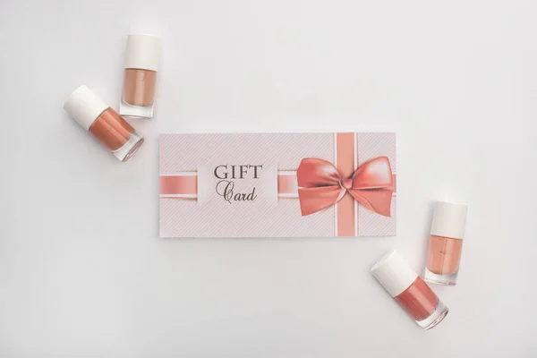 Vue du dessus des vernis à ongles et carte cadeau avec noeud sur fond blanc — Photo de stock