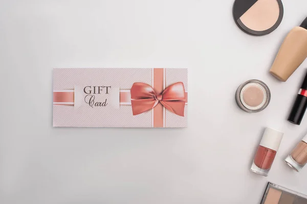 Vista superior de la tarjeta de regalo cerca de cosméticos decorativos en la superficie blanca — Stock Photo