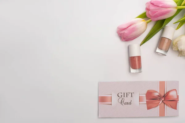 Top view of gift card near nail polishes and flowers on white surface — Stock Photo
