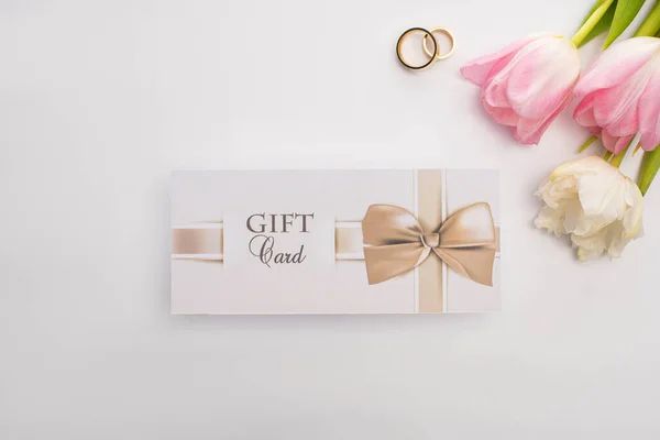 Vista superior de flores, anillos de boda y tarjeta de regalo sobre fondo blanco - foto de stock