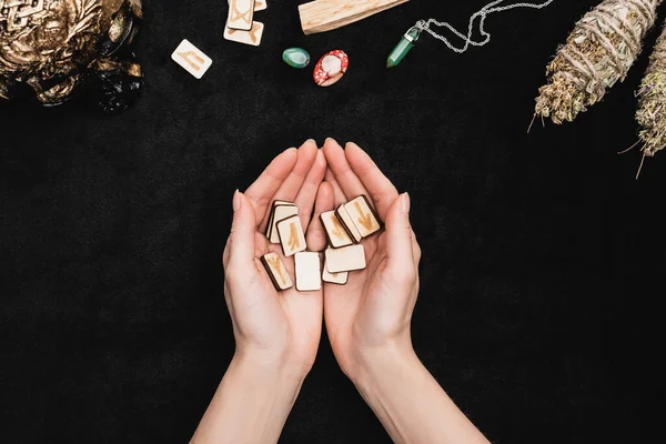 Top view of woman holding runes near amulets, crystals and voodoo skull on black — Stock Photo