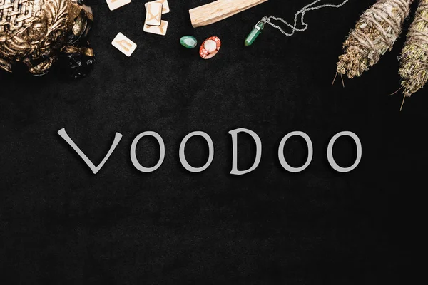 Top view of voodoo lettering near runes, amulets and crystals on black — Stock Photo