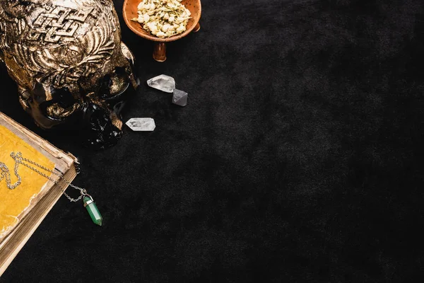 Top view of dried herb in bowl near occult voodoo skull and crystals on black — Stock Photo