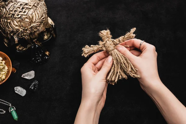 Верхний вид ведьмы, держащей куклу вуду рядом с черепом и кристаллами на черном — стоковое фото