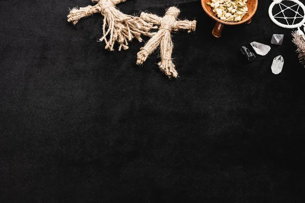 Top view of voodoo dolls near sagebrush in bowl, pentagram and crystals on black — Stock Photo