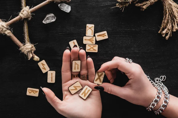 Vista dall'alto della donna che tiene le rune in mano vicino ai cristalli sul nero — Stock Photo