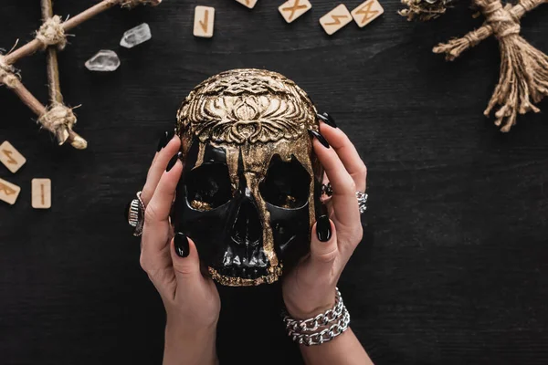 Top view of witch holding skull near runes, crystals and voodoo doll on black — Stock Photo