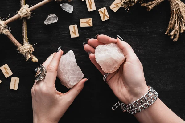 Top view of witch holding crystals near runes on black — Stock Photo