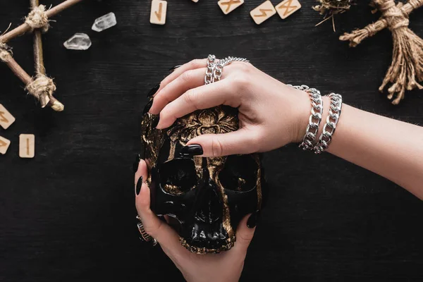 Cropped view of woman holding skull near crystals and runes on black — Stock Photo