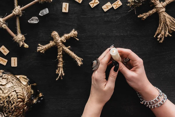 Vista dall'alto della donna che tiene la candela accesa vicino a bambole voodoo, rune, cristalli e teschio sul nero — Foto stock