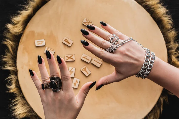 Top view of hands of evil witch above runes on wooden surface — Stock Photo