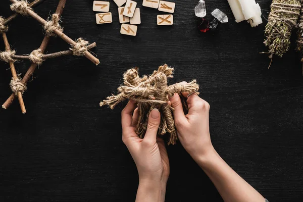 Top view of woman holding voodoo dolls near scandinavian runes, pentagram, candles and crystals on black — Stock Photo