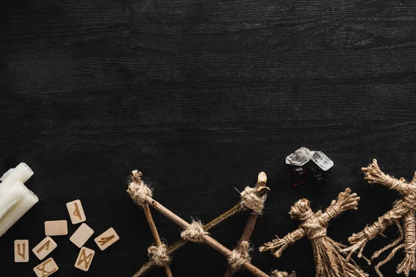 Top view of voodoo dolls, ancient runes, pentagram, crystals and candles on black — Stock Photo