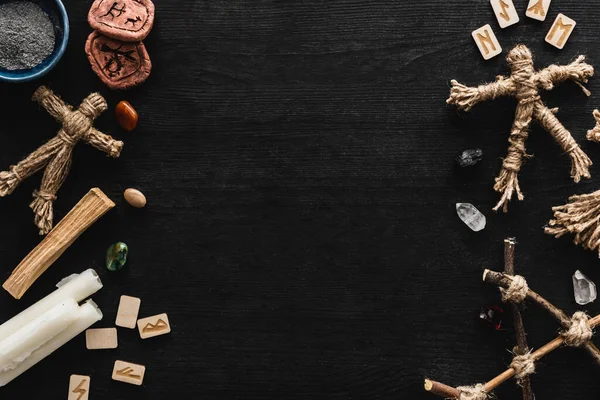 Vista dall'alto di bambole voodoo vicino ciotola con ceneri, candele, pietre e vecchie rune su nero — Stock Photo