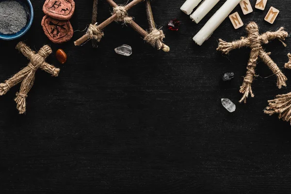 Top view of voodoo dolls near bowl with ashes, crystals, candles and old runes on black — Stock Photo