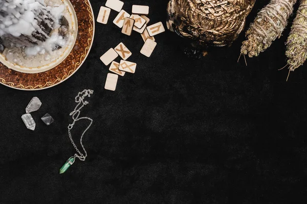 Top view of skull and dried herbs near runes, wax on candle and crystals on black — Stock Photo