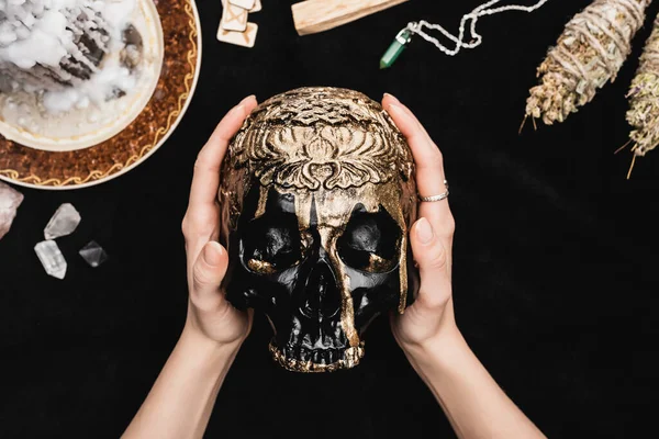 Top view of witch holding skull near runes, candle and crystals on black — Stock Photo
