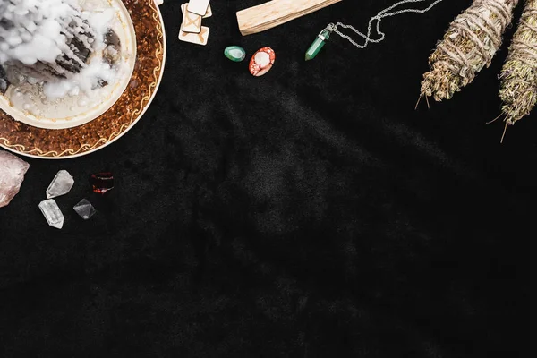 Top view of skull and dried herbs near old runes, wax on candle and crystals on black — Stock Photo