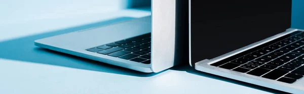 Modern open laptops with blank screen on blue workplace, panoramic shot — Stock Photo