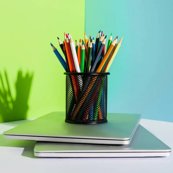 Porta-lápis com lápis de cor em laptops modernos em fundo azul, verde e branco — Fotografia de Stock