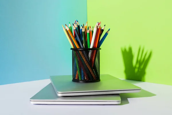 Porta-lápis com lápis de cor em laptops modernos em fundo azul, verde e branco — Fotografia de Stock