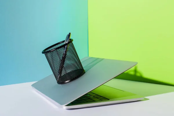 Pluma en el soporte de la computadora portátil moderna sobre fondo azul, blanco y verde - foto de stock