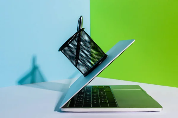 Pluma en el soporte de la computadora portátil moderna sobre fondo azul, blanco y verde - foto de stock